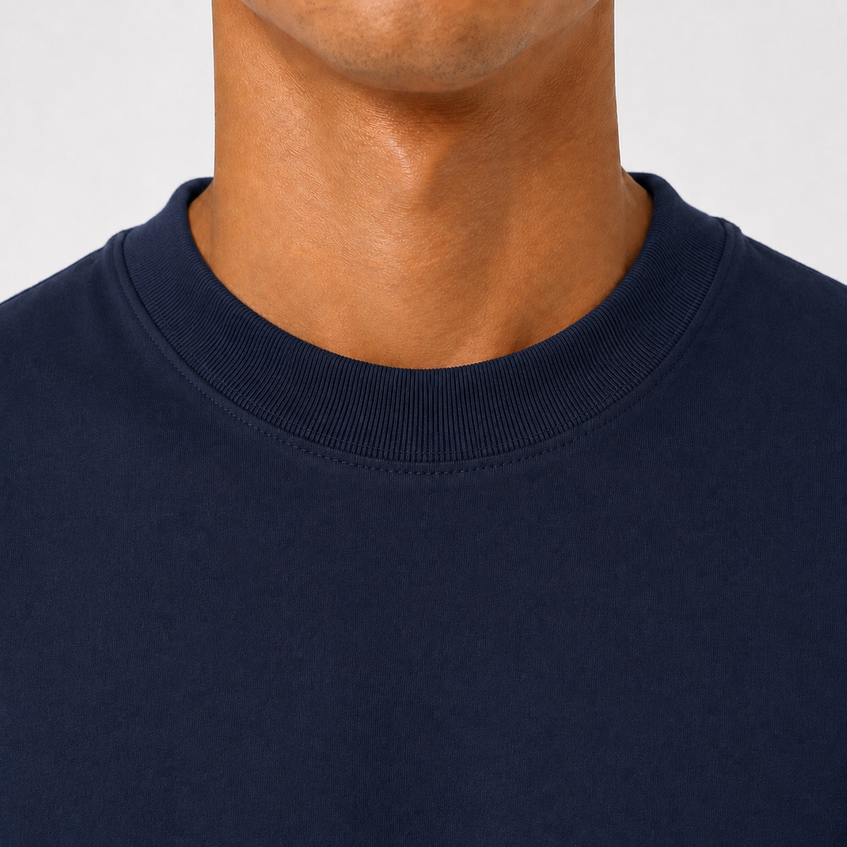 Close-up of a person's neck and lower face wearing a dark navy crew-neck t-shirt against a light gray background.