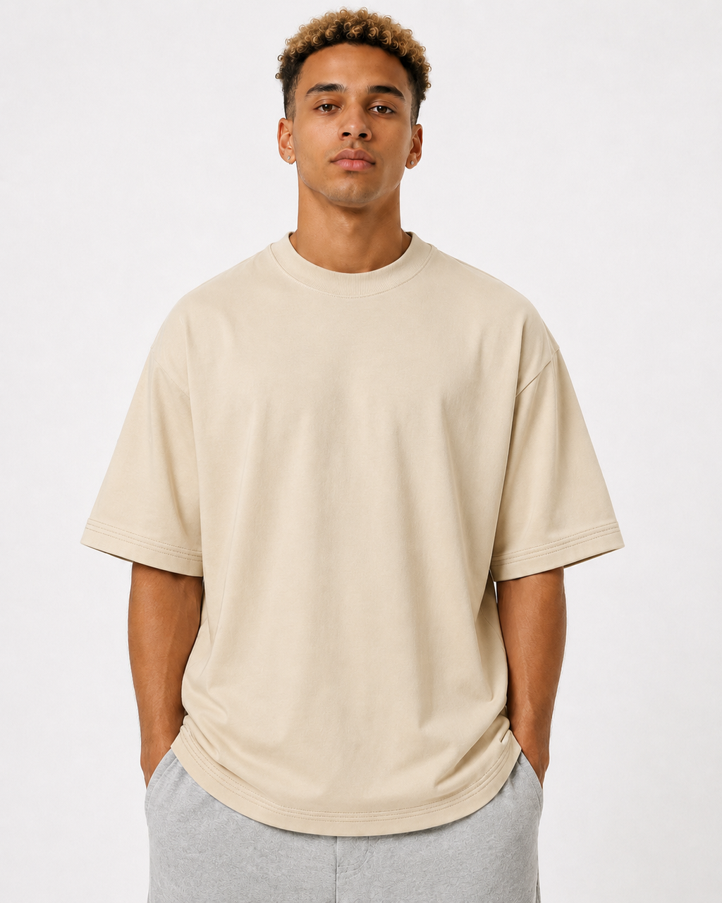 A man wearing an oversized beige 300GSM crewneck t-shirt and light gray sweatpants, standing against a plain white studio background.