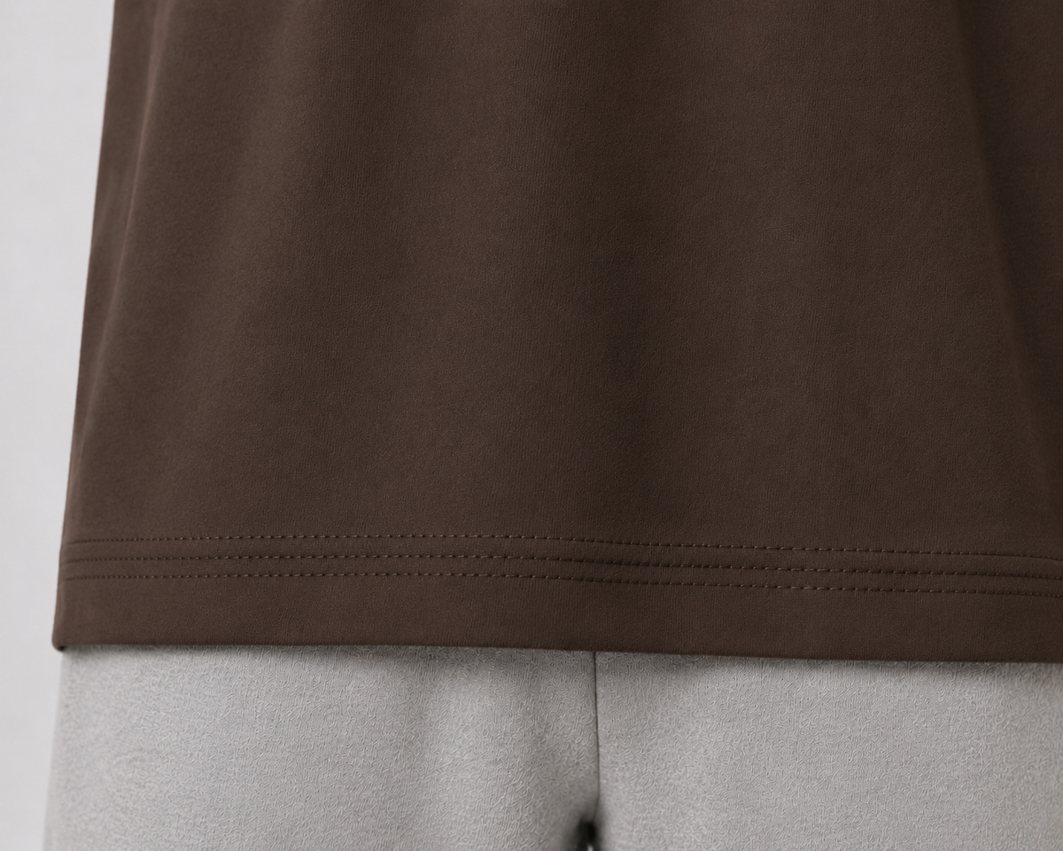 Close-up of a dark brown t-shirt hem with double stitching, shown on a light gray mannequin torso.
