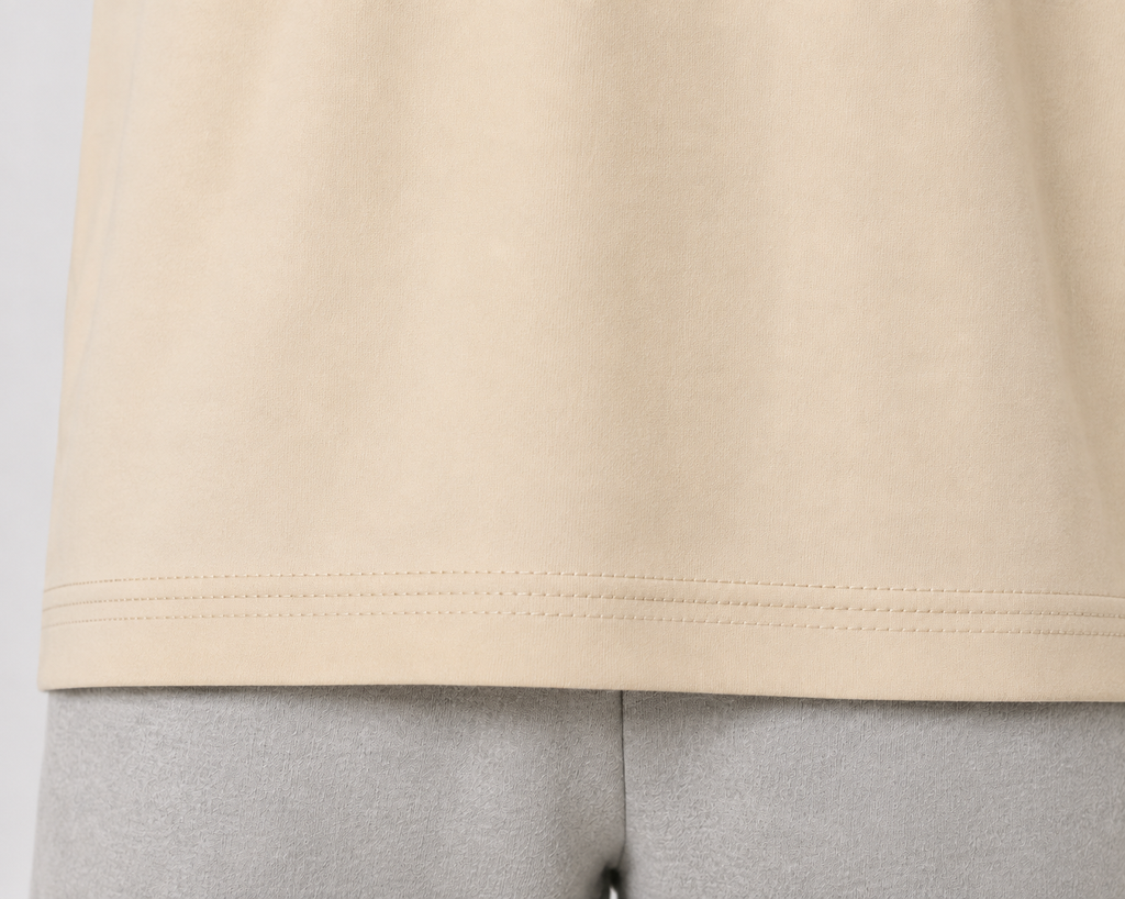 Close-up of a light beige or cream-colored knit garment hem with double stitching, shown on a mannequin or dress form against a light gray background.