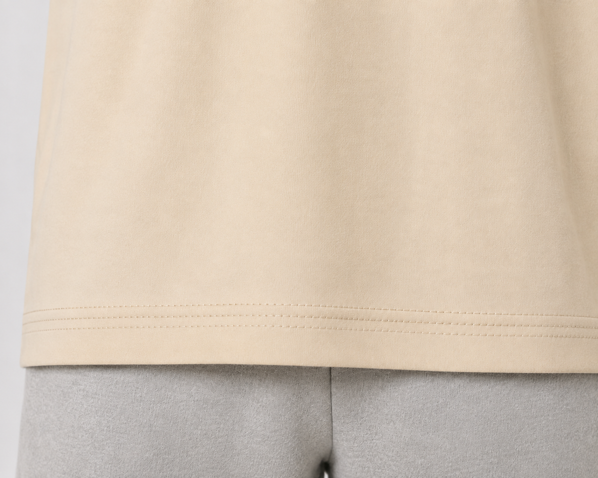 Close-up of a light beige or cream-colored knit garment hem with double stitching, shown on a mannequin or dress form against a light gray background.