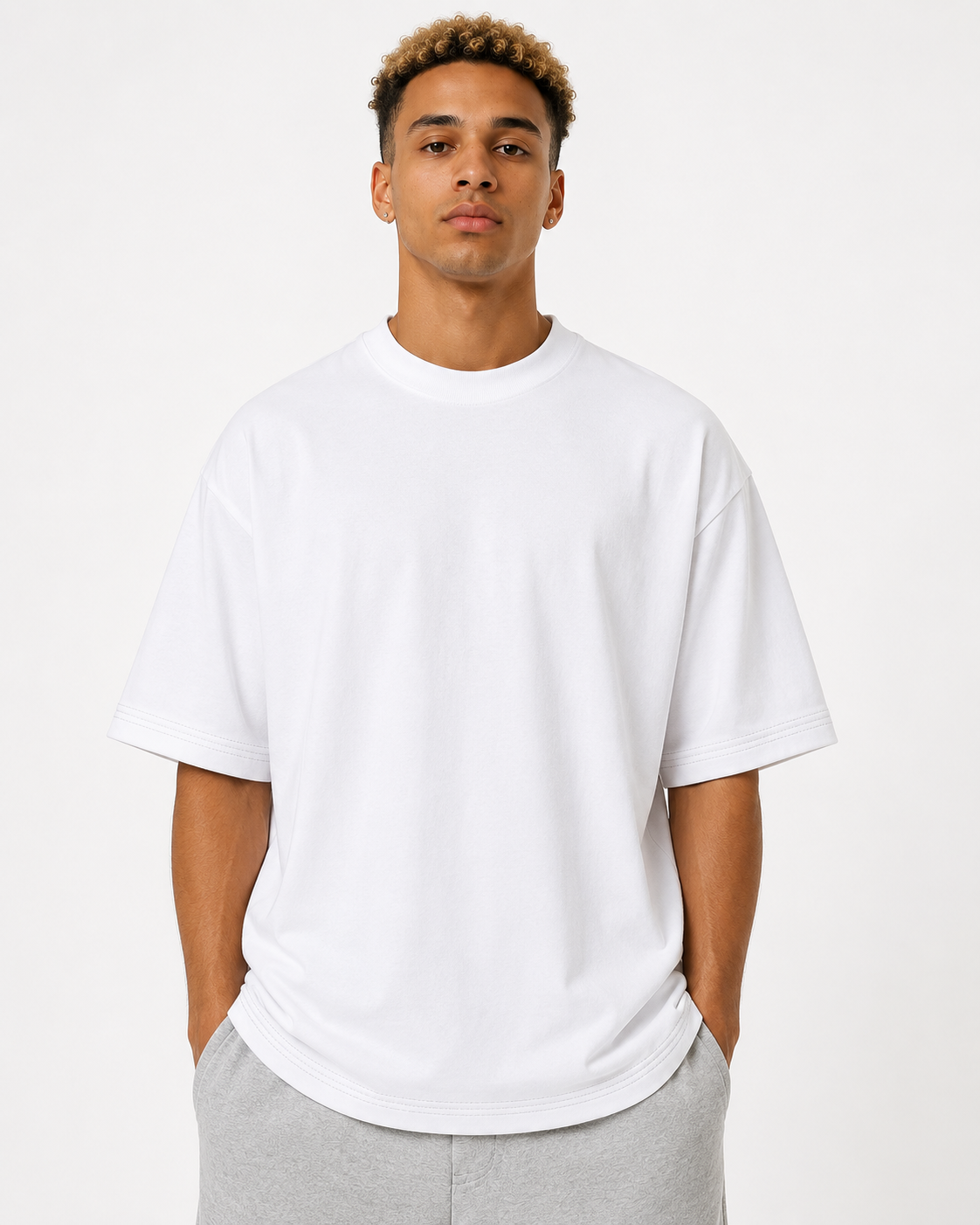 A man wearing a plain white short-sleeve crewneck t-shirt and light gray sweatpants, standing against a solid off-white studio background.