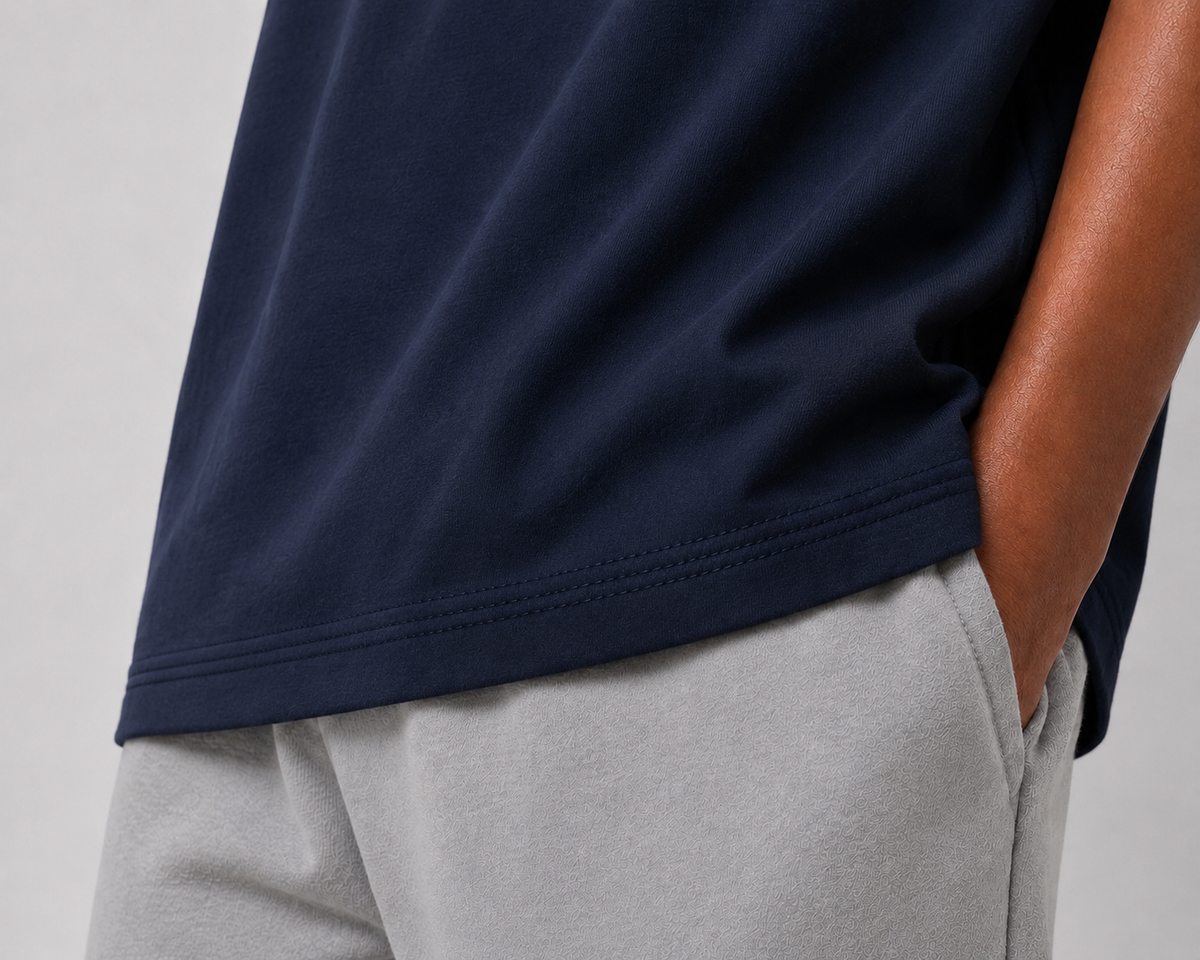 Close-up of a person wearing a navy blue short-sleeve top and light gray sweatpants, with the navy hem and side seam visible against a plain light gray background.