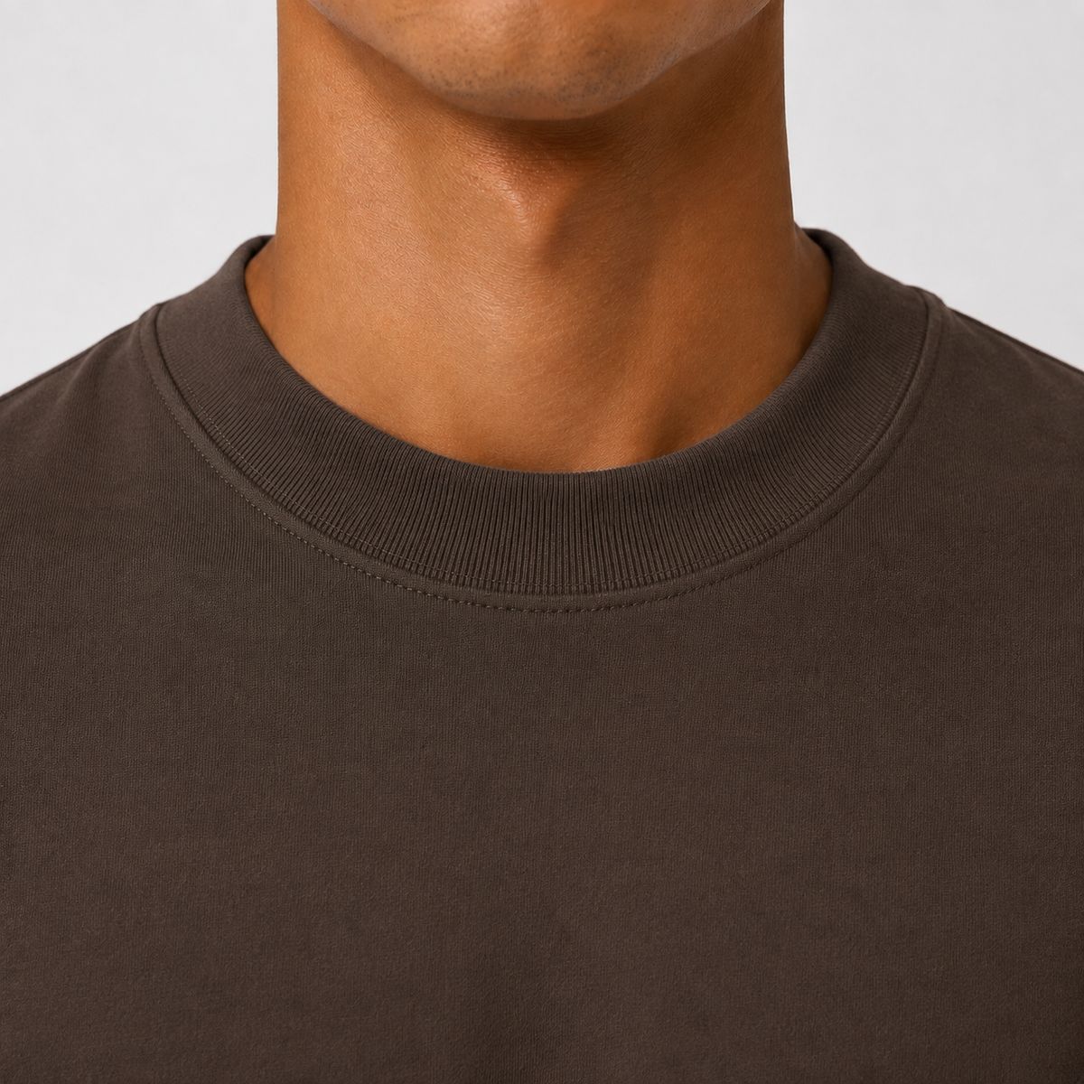Close-up of a person wearing a dark brown crew-neck t-shirt, showing the ribbed collar and chest area against a light gray background.