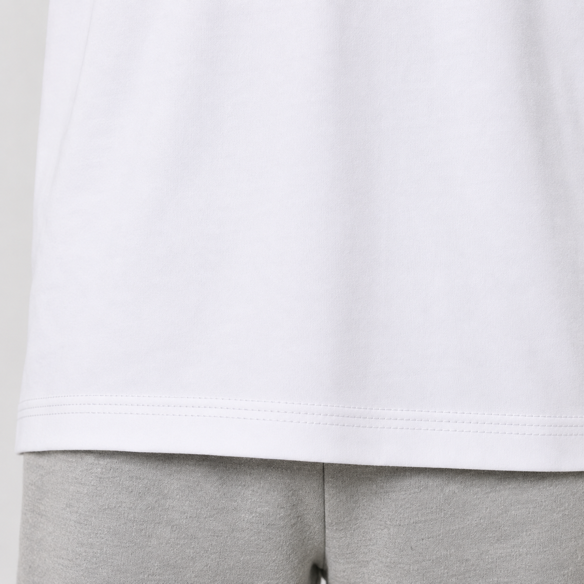 Close-up of a white short-sleeve top hem with gray sweatpants below, showing the stitched edge and fabric texture.