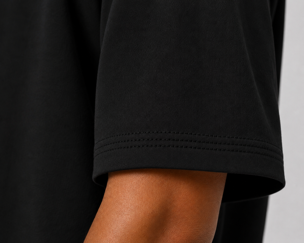 Close-up of a black short-sleeve t-shirt sleeve with double-stitched hem, worn on a model's arm against a light gray background.