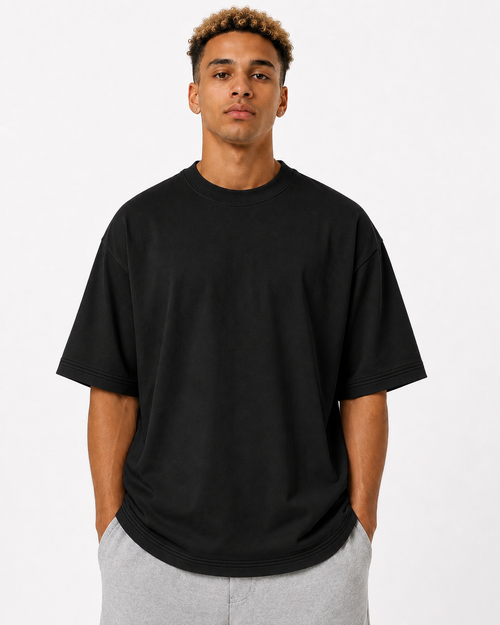 A man wearing an oversized black short-sleeve crewneck t-shirt and light gray sweatpants, standing against a plain white studio background.